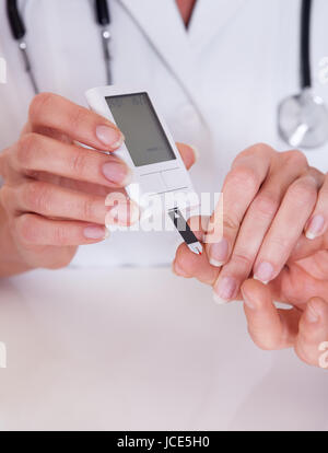 Test medico pazienti un livello di glucosio dopo la puntura il suo dito per disegnare una goccia di sangue e quindi usando un glycometer digitale Foto Stock