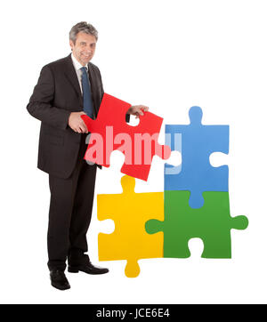 Imprenditore senior di assemblaggio di un puzzle. Isolato in bianco Foto Stock