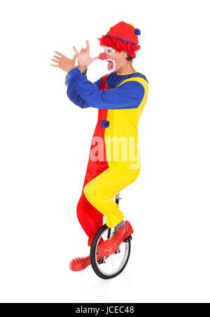 Ritratto di un divertente Clown eseguendo sul monociclo su sfondo bianco Foto Stock