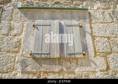 Una finestra chiusa con persiane di legno, costruito in un muro di pietra, stile mediterraneo. Croazia Foto Stock