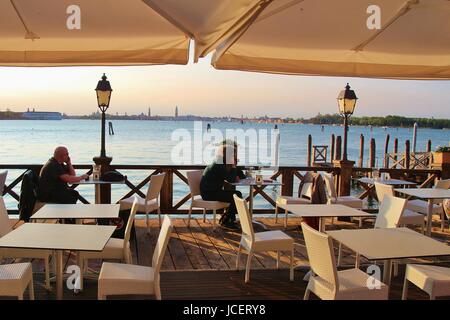 Giardino romantico ristorante dell'isola del Lido di Venezia. Gli uomini in attesa per i loro partner, sullo sfondo la skyline di Venezia. L'Italia, l'Europa. Foto Stock