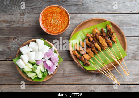 Vista aerea malese sate di pollo con deliziosa salsa di arachidi, ketupat, la cipolla e il cetriolo sul tavolo da pranzo in legno, uno dei famosi piatti della cucina locale. Foto Stock