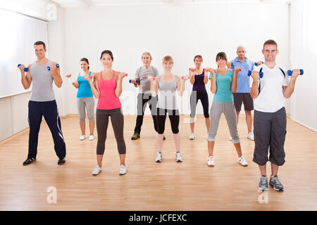 Lezione di aerobica di diversi uomini e donne di diversa età che lavora fuori in una palestra con pesi flettendo i loro muscoli del braccio Foto Stock