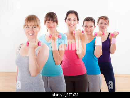 Lezione di aerobica di diverse donne di diversa età che lavora fuori in una palestra con pesi flettendo i loro muscoli del braccio Foto Stock