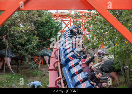 La gente a cavallo su un roller coaster, braccia verso l'alto, rendendo le facce Foto Stock