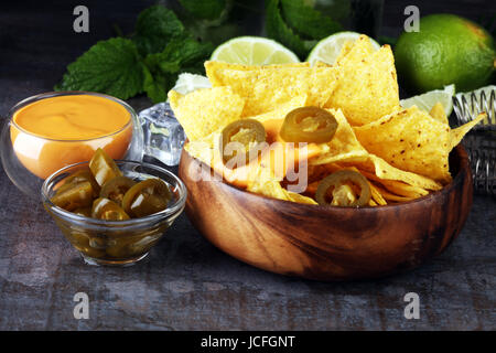 Una piastra di deliziose tortillas nachos con formaggio fuso di salsa su sfondo scuro Foto Stock