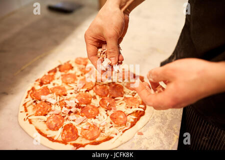 Cuocere le mani aggiungendo prosciutto ai salami pizza in pizzeria Foto Stock