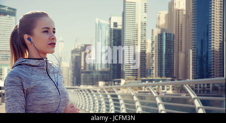 Donna felice con gli auricolari in esecuzione su Dubai City Foto Stock