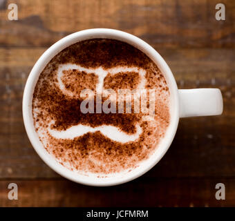 Primo piano di una tazza di cappuccino con un paio di occhiali e un baffi disegnati con il cacao in polvere sulla sua schiuma Foto Stock