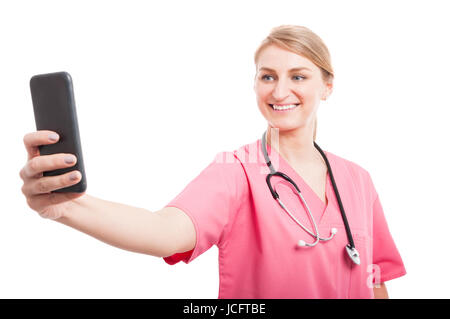 Infermiera femmina indossando scrubs tenendo selfie con lo smartphone e sorridente isolati su sfondo bianco Foto Stock