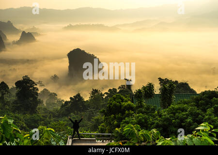 Uomo in piedi sul banco di lavoro e alzando la mano per vedere la vista del rurale con ambiente di nebbia. Foto Stock