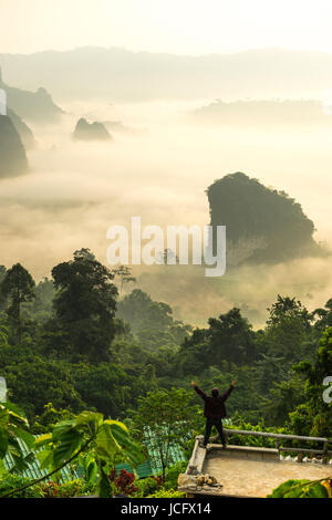 Uomo in piedi sul banco di lavoro e alzando la mano per vedere la vista del rurale con ambiente di nebbia. Foto Stock