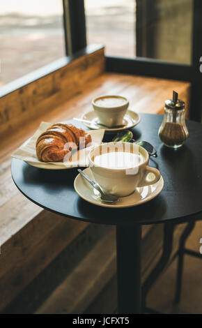 Caffè latte, cappuccino e cornetto sul tavolino in cafe, francese o italiano concetto colazione Foto Stock