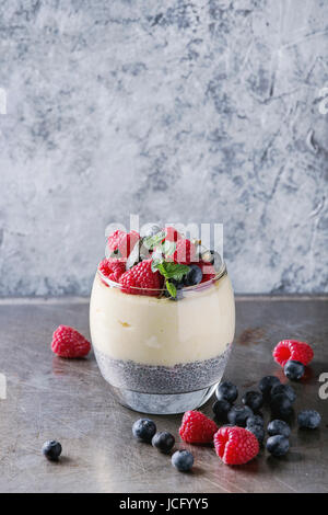 La prima colazione dolce a strati semi di chia pudding, farinata di riso in vetro decorato da mirtilli freschi, lampone, menta. Stare in piedi sul grigio Sfondo texture Foto Stock