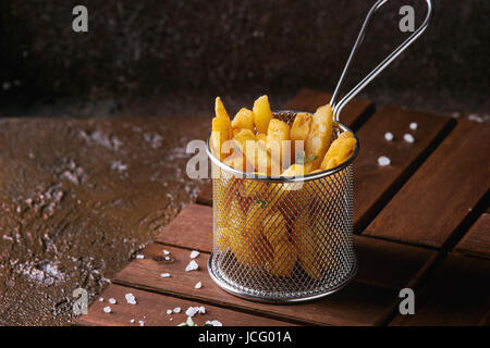 Tradizionali di patatine fritte patate servita nel cestello con sale, il timo sulla tavola di legno marrone su sfondo di texture. In casa il fast food Foto Stock