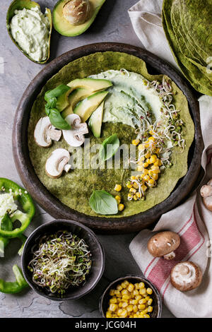 Gli spinaci Verde matcha tortilla con vegan ingredienti per il ripieno. Il mais dolce, avocado, paprica verde, germogli di funghi servita nella piastra di terracotta ov Foto Stock