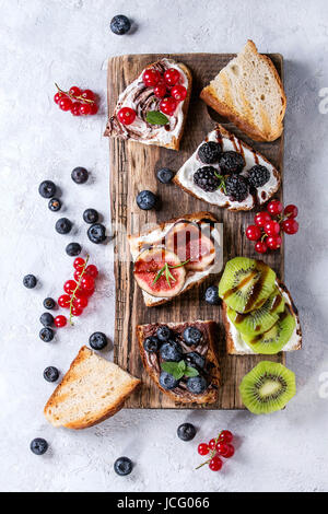 Varietà di panini dolci con frutti di bosco e crema di formaggio e cioccolato di swirl. Ribes rosso, mirtilli e kiwi a fette, fichi a servire la scheda sopra whi Foto Stock