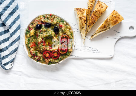 Baba ganoush fatta con melanzane arrosto, il peperone rosso e le erbe ma nessun tahini fotografato su una lavagna bianca dalla vista dall'alto. Pita fette sono sulla s Foto Stock