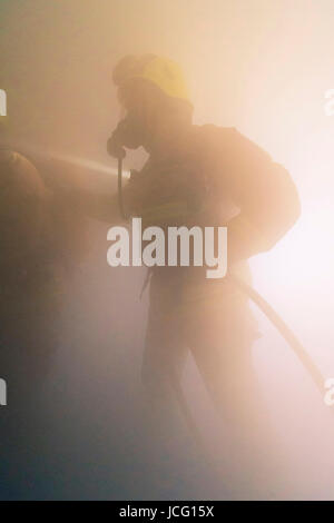 Fireman indossando apparecchi respiratori e portante un manicotto flessibile di entrare in una piena di fumo in camera una casa d'abitazione. Foto Stock