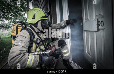 I vigili del fuoco di indossare respiratore e portante un manicotto flessibile di entrare in una piena di fumo in camera una casa d'abitazione. Foto Stock