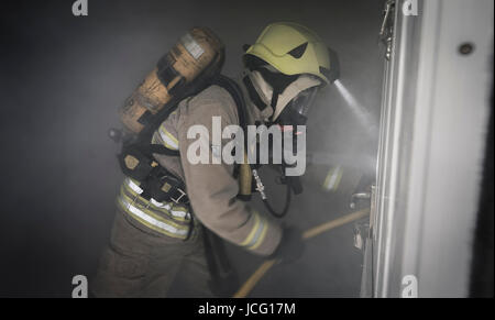 I vigili del fuoco di indossare respiratore e portante un manicotto flessibile di entrare in una piena di fumo in camera una casa d'abitazione. Foto Stock