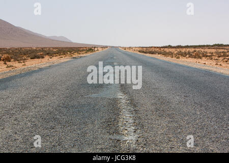 Strada diritta attraverso il deserto nella regione di Tata, montagne sullo sfondo. Il Marocco, Africa Foto Stock