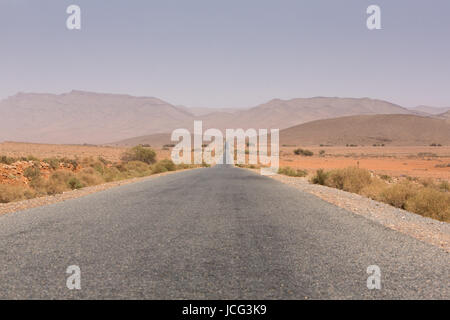 Strada diritta attraverso il deserto nella regione di Tata, montagne sullo sfondo. Il Marocco, Africa Foto Stock