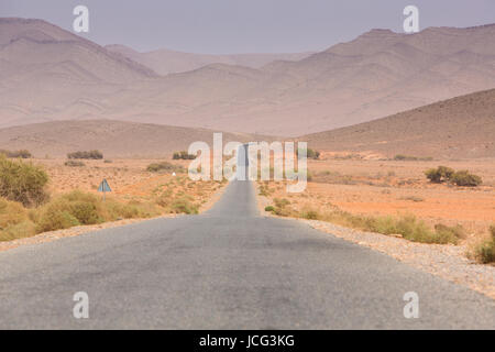 Strada diritta attraverso il deserto nella regione di Tata, montagne sullo sfondo. Il Marocco, Africa Foto Stock