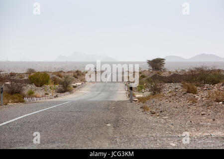 Strada diritta attraverso il deserto nella regione di Tata, montagne sullo sfondo. Il Marocco, Africa Foto Stock