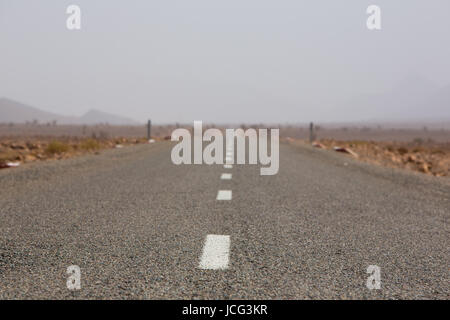 Strada diritta attraverso il deserto nella regione di Tata, montagne sullo sfondo. Il Marocco, Africa Foto Stock