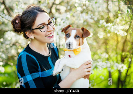 Felice giovane donna abbracciando e divertirsi con il suo Jack Russell Terrier nel giardino fiorito Foto Stock