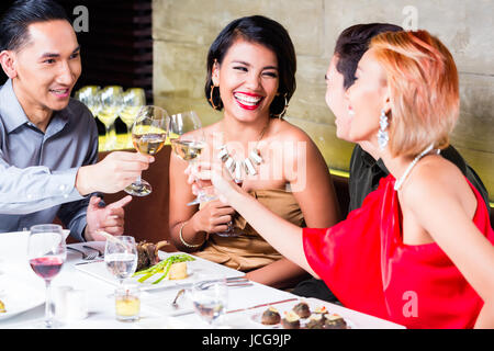 Amici asiatici, due coppie, a pranzo nel ristorante elegante mangiare bene e bere il vino Foto Stock