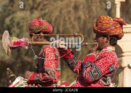 Uomo in tunica colorata a soffiare una tromba mentre a dorso di un cammello in una sfilata all'inizio dell'annuale Festival del deserto in Jaisalmer, Rajasthan, India. Foto Stock