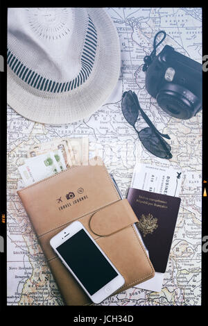 Fotocamera istantanea, telefono cellulare (con schermo nero), occhiali da sole, valute diverse e cappello bianco su un'antica mappa, concetto di viaggio, verticale Foto Stock