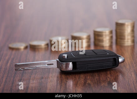 Close-up di chiave Auto nella parte anteriore delle monete impilate su un tavolo di legno Foto Stock