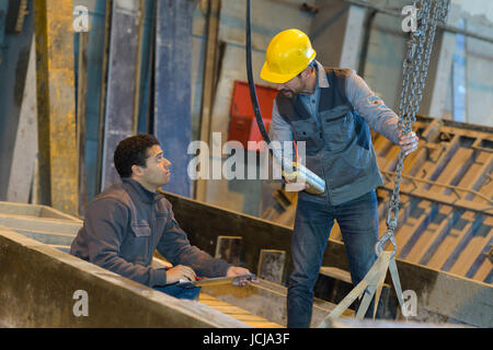 Regolazione dei lavoratori una puleggia grande gancio in una fabbrica Foto Stock