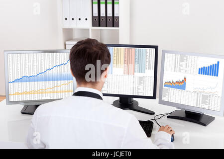 Al di sopra della spalla vista degli schermi di computer di uno stock broker trading in un mercato rialzista che mostra grafici ascendente Foto Stock
