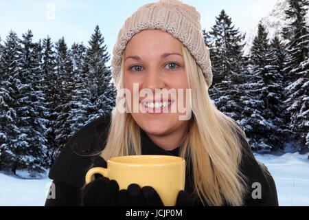 Junge blonde Frau draußen im Wald beim Trinken einer Tasse Tee im inverno Foto Stock