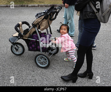 I turisti giapponesi sono disponibili in tutte le dimensioni e di questa incantevole piccola ragazza vestita in rosa era occupato spingendo il suo passeggino mentre sua madre visto un attrazione.. Foto Stock