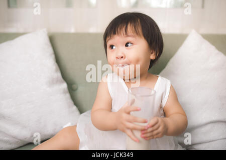 Carino bambina bere latte con baffi di latte a casa Foto Stock