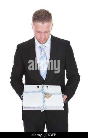 Imprenditore tenendo un top secret file confidenziali bloccato con una catena e un lucchetto per impedire accessi non autorizzati isolato su bianco Foto Stock