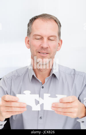 Ritratto di un imprenditore maturo risolvere puzzle in Office Foto Stock