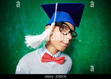 Carino schoolboy in occhiali e graduazione hat guardando la fotocamera Foto Stock