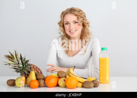 Sorridente donna bionda seduta con frutti sul tavolo Foto Stock