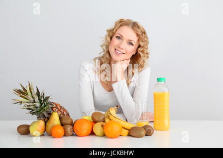 Sorridente donna bionda seduta con frutti sul tavolo Foto Stock