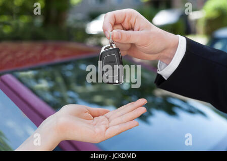 Immagine ritagliata del venditore di consegnare la chiave per donna dalla nuova vettura Foto Stock