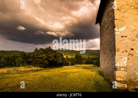 Paesaggio con prato e bosco Thunderclouds dietro un vecchio edificio Foto Stock