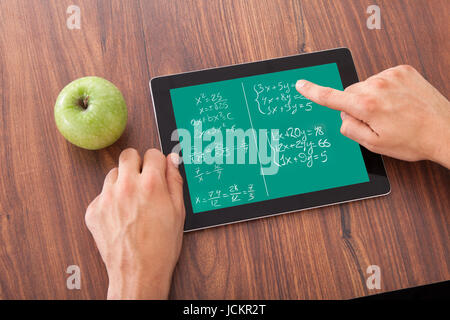 Immagine ritagliata di giovani studenti di sesso maschile la soluzione matematica del problema sulla tavoletta digitale da mela verde sul tavolo Foto Stock