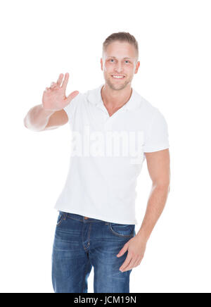 Montare amichevole muscolare di giovane uomo in jeans e una maglietta in piedi agitando la mano nel saluto o dire addio isolato su bianco Foto Stock