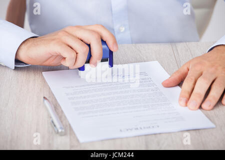 Immagine ritagliata di imprenditore di timbratura carta contratto alla scrivania in ufficio Foto Stock